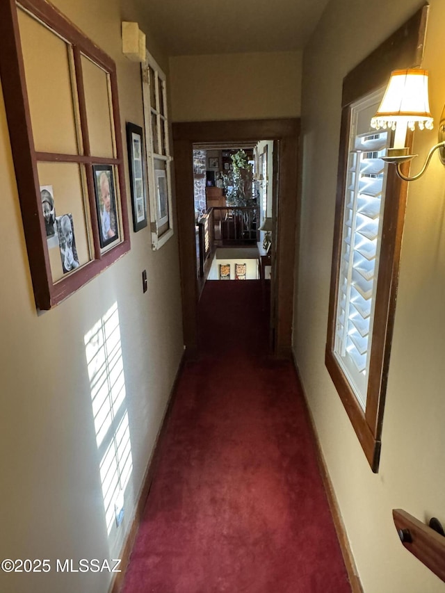 hallway with baseboards and dark carpet