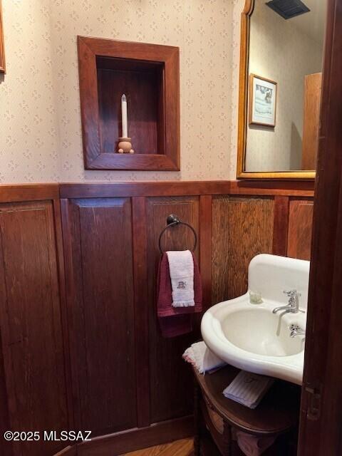 bathroom featuring a wainscoted wall, a sink, and wallpapered walls