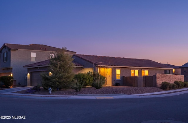 view of front of house featuring stucco siding, a tile roof, fence, and driveway