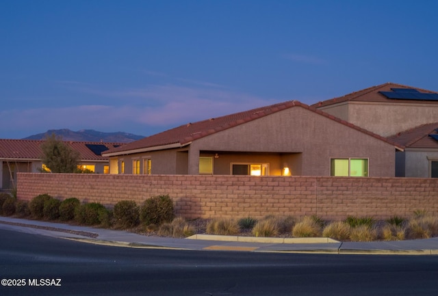 property exterior at dusk featuring stucco siding, a tile roof, fence, and a mountain view