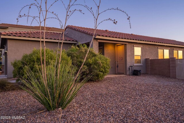 back of property with a tile roof, stucco siding, and fence
