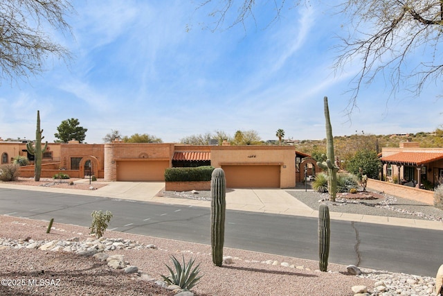 pueblo-style house with concrete driveway, a garage, and stucco siding