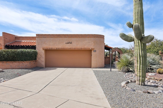 pueblo-style house with stucco siding, an attached garage, a tile roof, and driveway