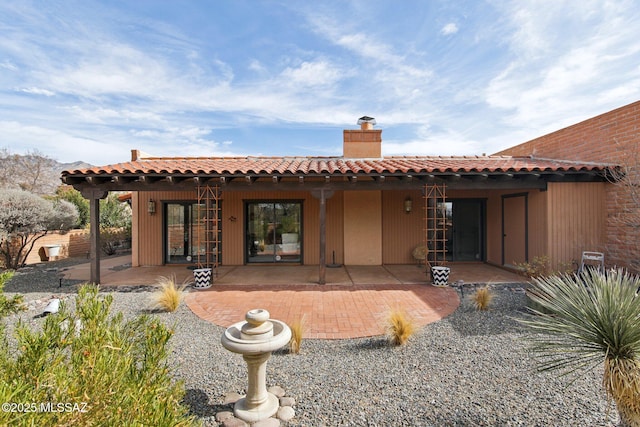 back of property with a patio, a tiled roof, and a chimney