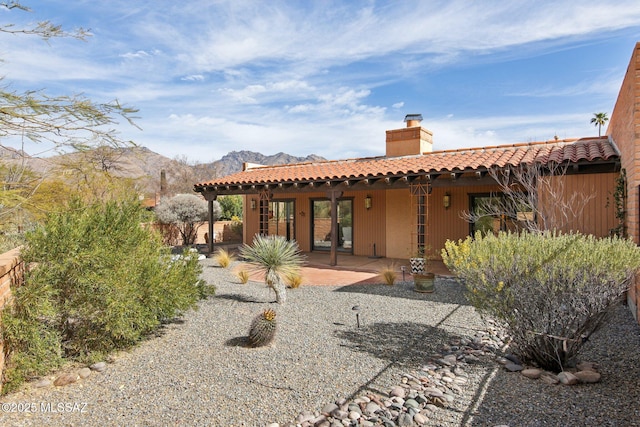 rear view of house with a patio, stucco siding, a chimney, a tile roof, and a mountain view