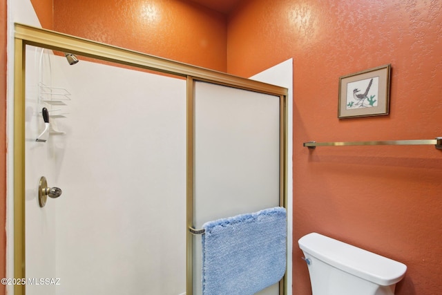 bathroom featuring toilet, a textured wall, and a shower with shower door