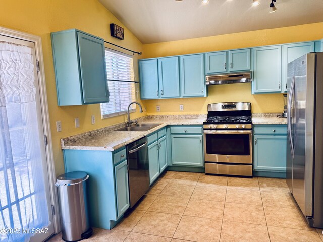 kitchen with appliances with stainless steel finishes, vaulted ceiling, under cabinet range hood, a sink, and light tile patterned flooring