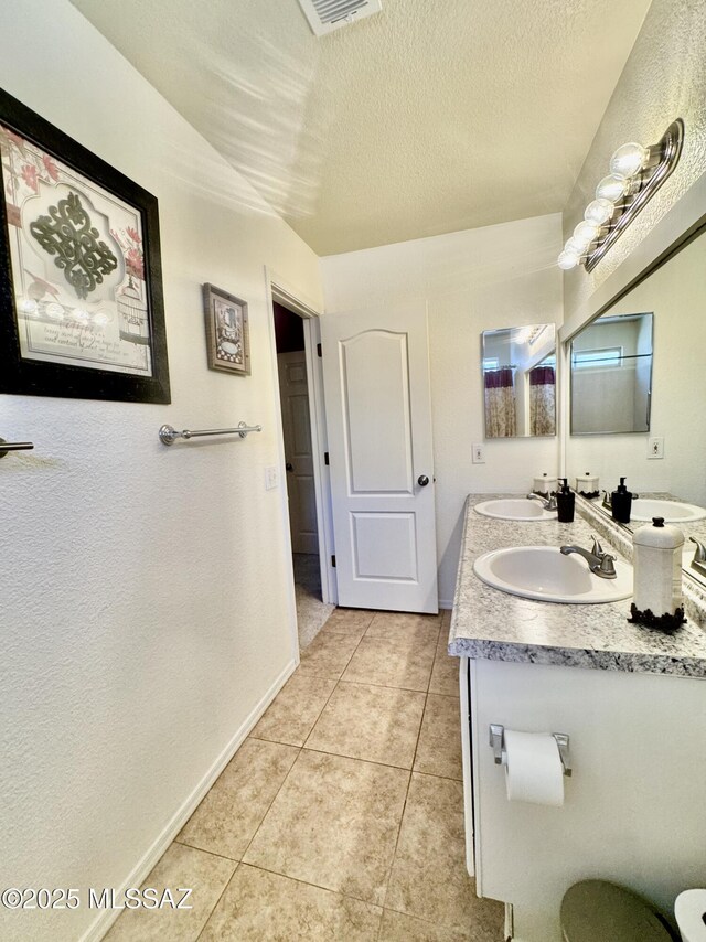 bathroom featuring tile patterned flooring, a textured ceiling, baseboards, and a sink