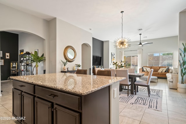 kitchen with light stone counters, arched walkways, open floor plan, and dark brown cabinets