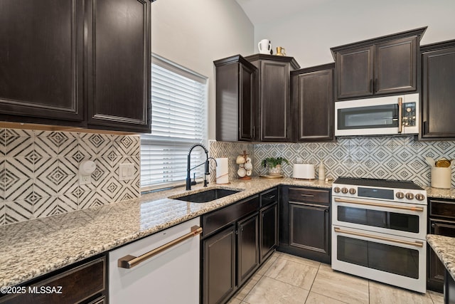 kitchen featuring light stone counters, a sink, backsplash, double oven range, and dishwasher