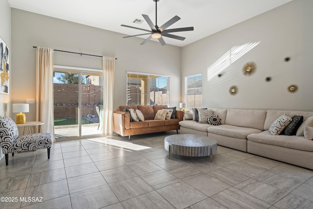 living area with a ceiling fan, a healthy amount of sunlight, visible vents, and a high ceiling