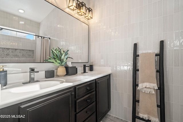 bathroom with double vanity, tiled shower, a sink, and tile walls