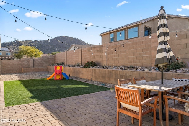 view of patio / terrace featuring a fenced backyard, a mountain view, a playground, and outdoor dining space