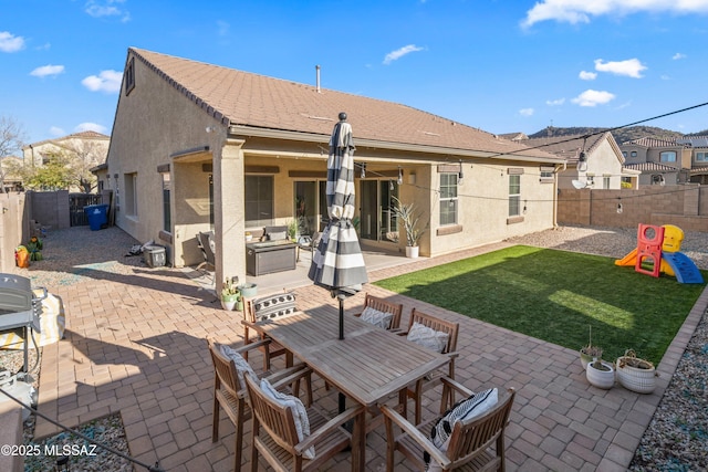 rear view of property featuring a lawn, a patio, outdoor dining area, a playground, and stucco siding