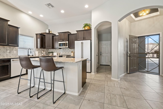 kitchen with dark brown cabinetry, white appliances, visible vents, a center island, and tasteful backsplash