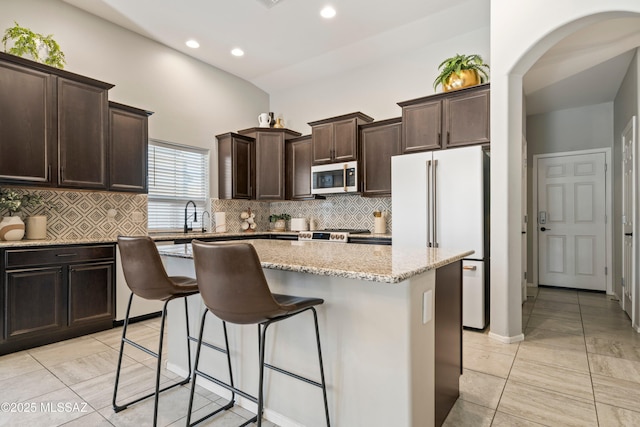 kitchen with dark brown cabinetry, a kitchen breakfast bar, freestanding refrigerator, a center island, and stainless steel microwave