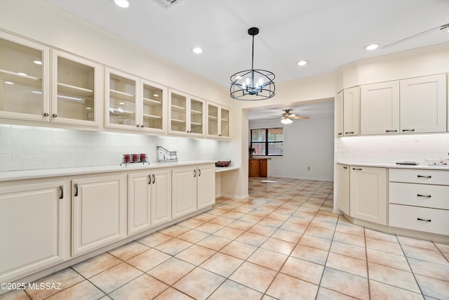 kitchen with tasteful backsplash, glass insert cabinets, ceiling fan, light countertops, and hanging light fixtures