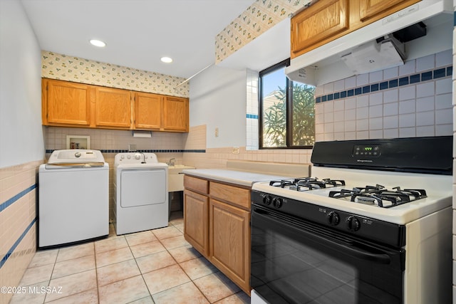 kitchen with washing machine and clothes dryer, under cabinet range hood, gas range, light countertops, and light tile patterned floors