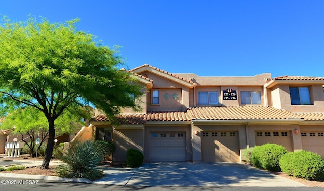 view of front facade with a tiled roof, stucco siding, an attached garage, and driveway