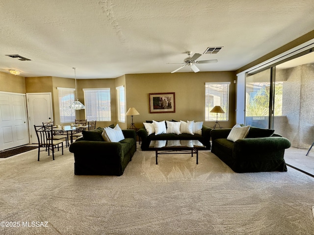 living room featuring visible vents, light colored carpet, a textured ceiling, and a ceiling fan