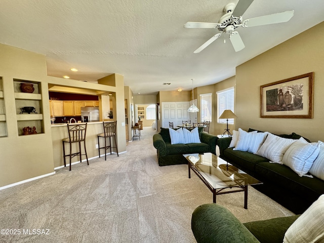 living area with baseboards, a textured ceiling, light carpet, and a ceiling fan