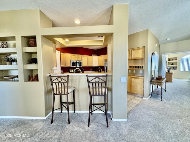 kitchen with built in features, a textured ceiling, a kitchen bar, stainless steel microwave, and light colored carpet