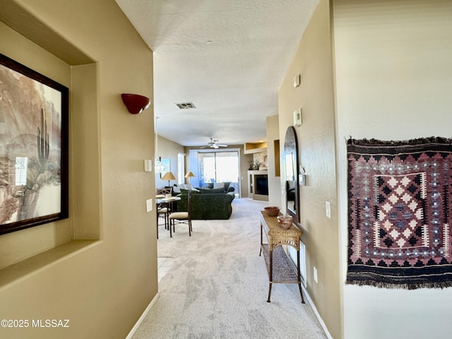 hall with baseboards, visible vents, a textured ceiling, and carpet