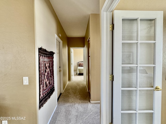 hallway with carpet flooring, a textured wall, and baseboards
