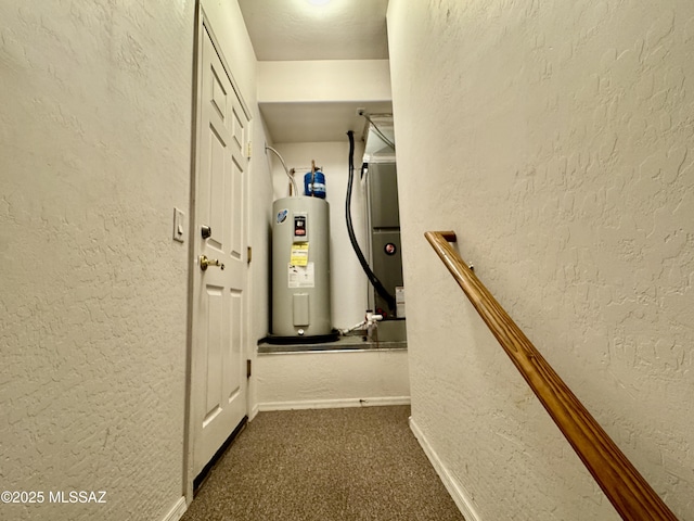hall featuring heating unit, a textured wall, baseboards, and electric water heater