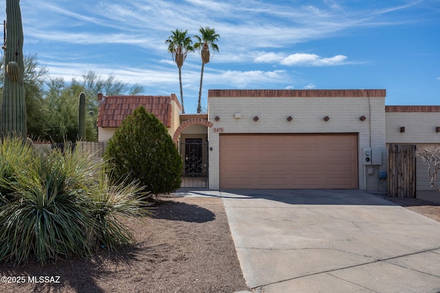 southwest-style home with concrete driveway, an attached garage, a tile roof, and fence