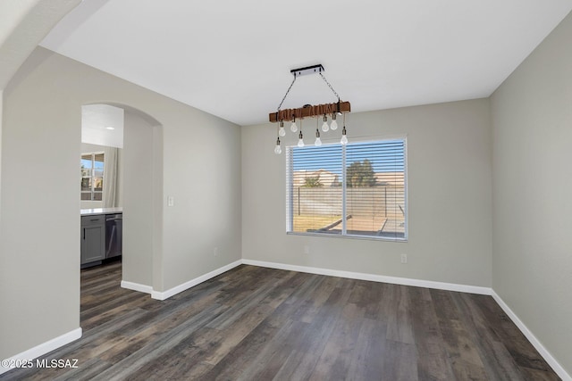 unfurnished dining area with arched walkways, dark wood finished floors, and baseboards