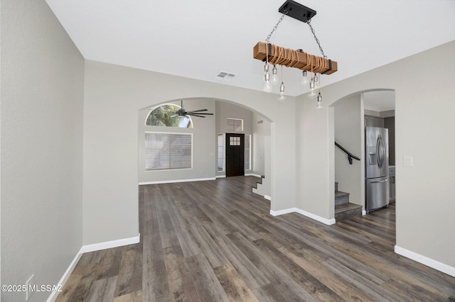 empty room with arched walkways, dark wood-style flooring, visible vents, baseboards, and stairs