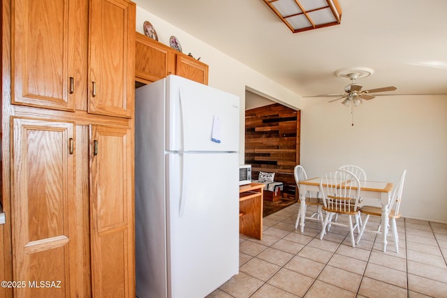 kitchen with light tile patterned floors, a ceiling fan, light countertops, freestanding refrigerator, and brown cabinetry