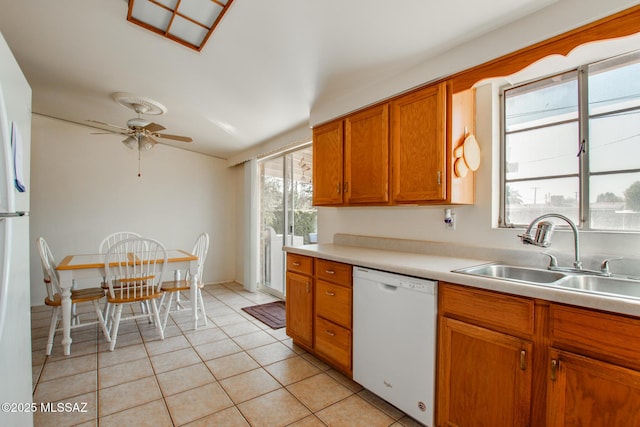 kitchen with light tile patterned floors, white dishwasher, a sink, light countertops, and brown cabinetry