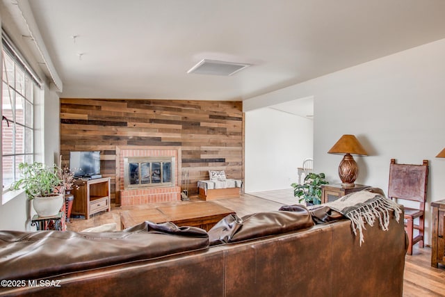 living room with light wood finished floors, wood walls, and a brick fireplace