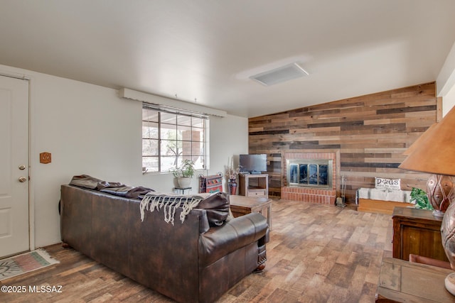 living area with vaulted ceiling, wood walls, a fireplace, and wood finished floors