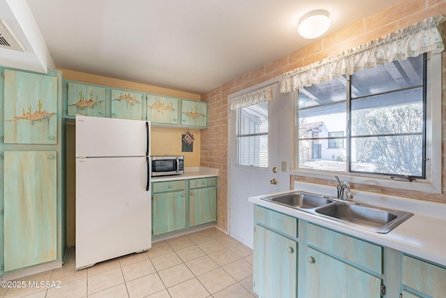 kitchen featuring light tile patterned floors, a sink, light countertops, freestanding refrigerator, and stainless steel microwave