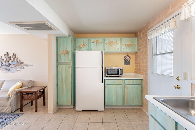 kitchen with visible vents, stainless steel microwave, freestanding refrigerator, light countertops, and light tile patterned flooring