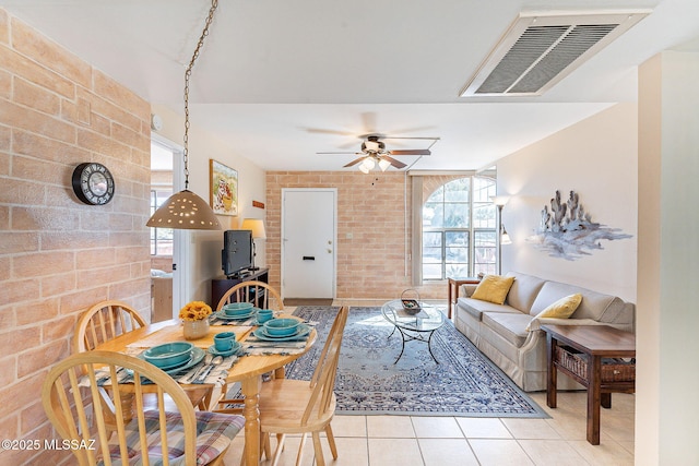 dining area featuring a ceiling fan, visible vents, brick wall, and light tile patterned floors