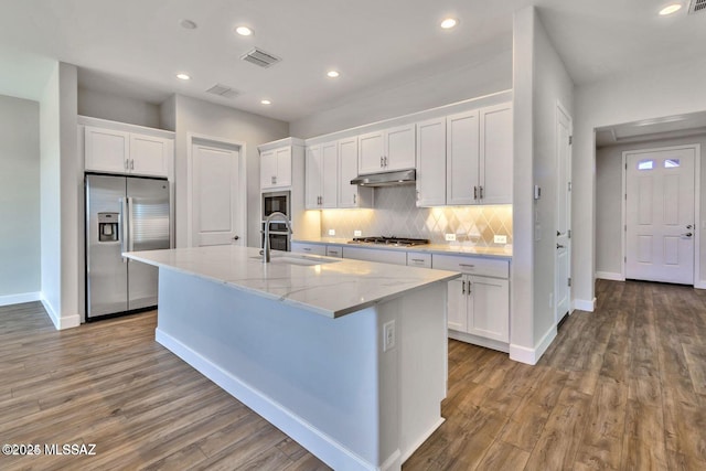 kitchen with white cabinets, decorative backsplash, stainless steel appliances, under cabinet range hood, and a sink