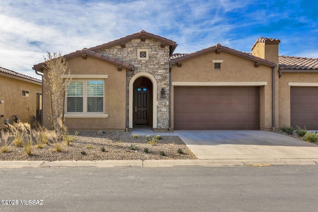 mediterranean / spanish-style house with stone siding, concrete driveway, an attached garage, and stucco siding