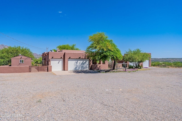 pueblo revival-style home featuring driveway, an attached garage, fence, and stucco siding