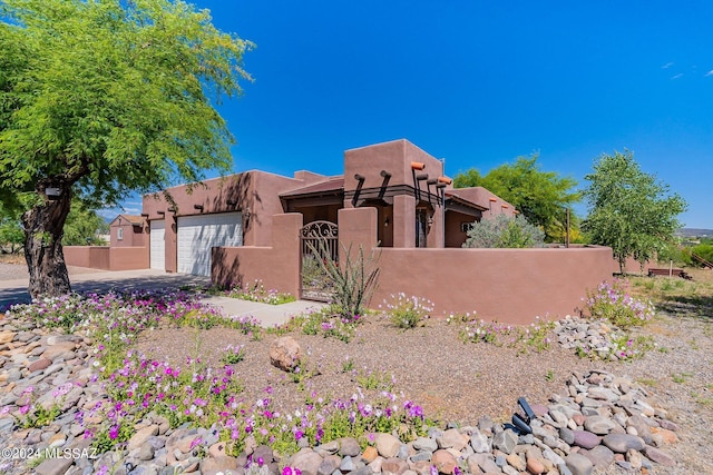 pueblo-style home featuring a garage, a fenced front yard, and stucco siding