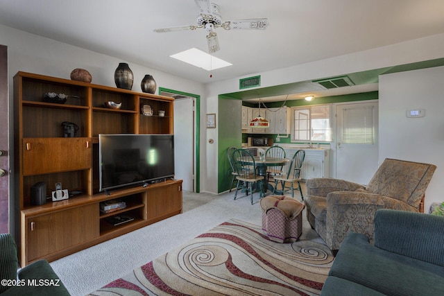 living area with a skylight, visible vents, a ceiling fan, and light colored carpet