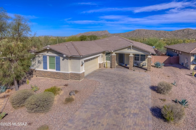 view of front of house with fence, an attached garage, stone siding, decorative driveway, and a mountain view