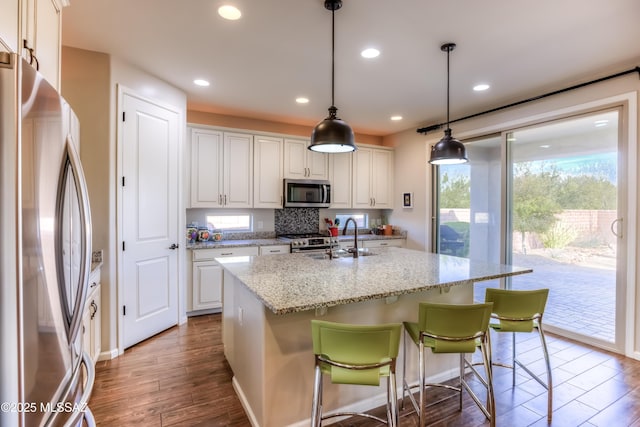 kitchen featuring a center island with sink, a sink, stainless steel appliances, white cabinets, and dark wood-style flooring