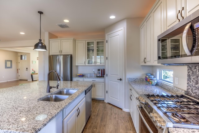 kitchen with glass insert cabinets, light wood-style flooring, hanging light fixtures, stainless steel appliances, and a sink