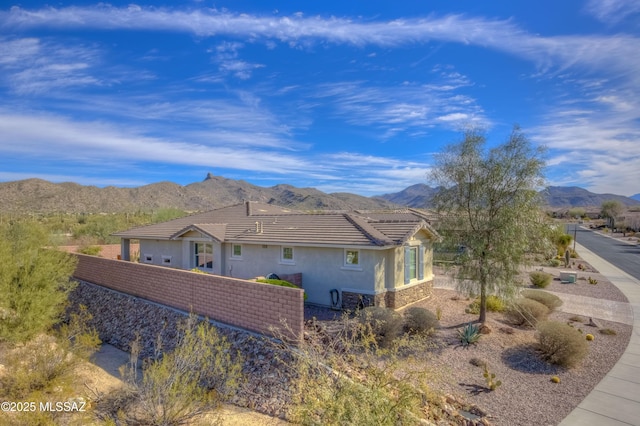 view of side of home with a tiled roof, a mountain view, stucco siding, and fence