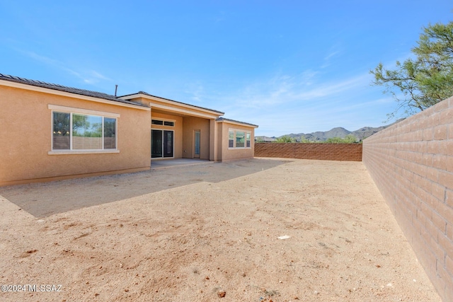 rear view of house with a fenced backyard, a mountain view, and stucco siding