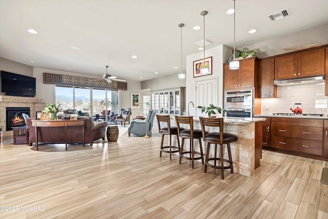 kitchen featuring visible vents, open floor plan, stainless steel appliances, decorative backsplash, and a tile fireplace